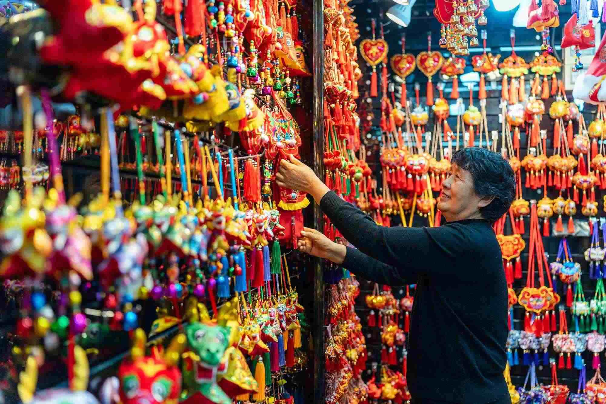 2023年12月11日，金華義烏國際商貿(mào)城，龍年喜慶用品掛滿攤位，顧客正在挑選中。