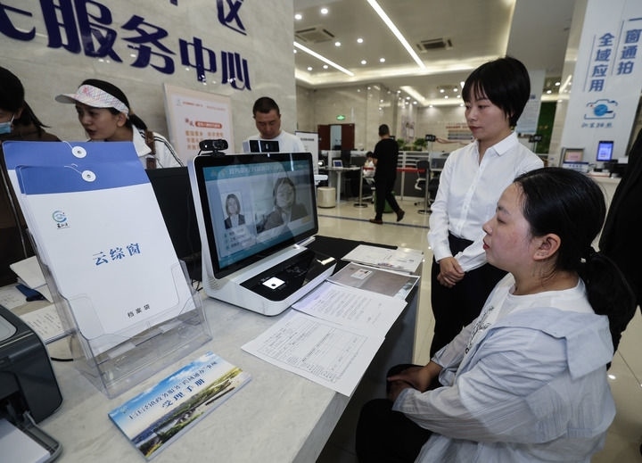 在浙江省嘉興市秀洲區(qū)王江涇鎮(zhèn)便民服務(wù)中心的“跨域通辦·云綜窗”窗口，辦理開業(yè)登記的個體工商戶（右一）通過該系統(tǒng)與江蘇省蘇州市吳江區(qū)盛澤鎮(zhèn)行政審批局工作人員視頻連線，進(jìn)行身份讀取及材料線上審核（2024年5月9日攝）。新華社記者 徐昱 攝