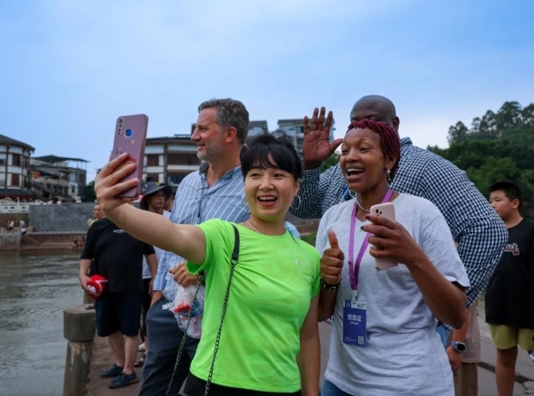 2024“一帶一路”媒體合作論壇聯(lián)合采訪調(diào)研行成員在樂山蘇稽古鎮(zhèn)與游客合影留念。本報記者 伊霄攝