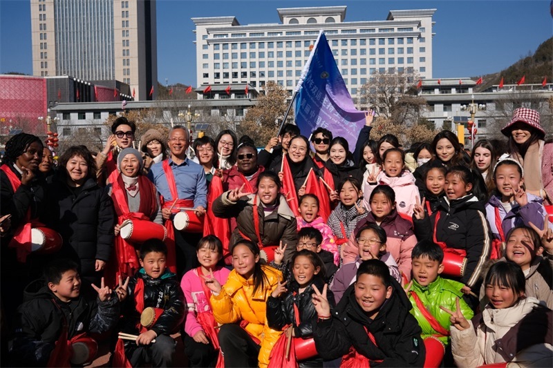 中外青年學子在安塞文化廣場觀看陜北腰鼓和大秧歌表演后合影留念，大家踏著鼓點共舞，翻飛的紅綢與躍動的身影交織，在黃土地廣場上繪出一幅生動的陜北民俗互動畫卷